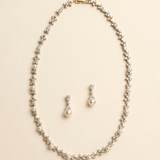 A gold necklace and earrings set are displayed against a light beige background.