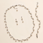 A necklace and earrings set made of white pearls and silver leaf-shaped charms are displayed on a light-colored background.