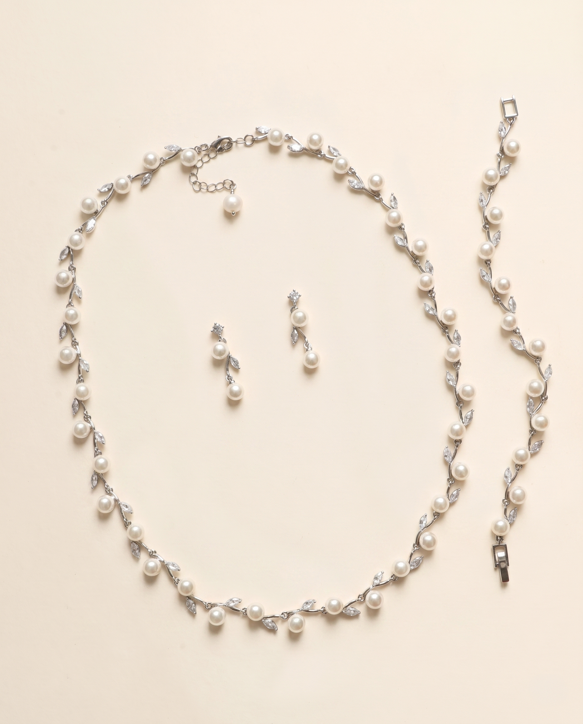 A necklace and earrings set made of white pearls and silver leaf-shaped charms are displayed on a light-colored background.