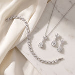 A delicate necklace, bracelet, and earrings are arranged on a white marble surface, creating an elegant and sophisticated display.