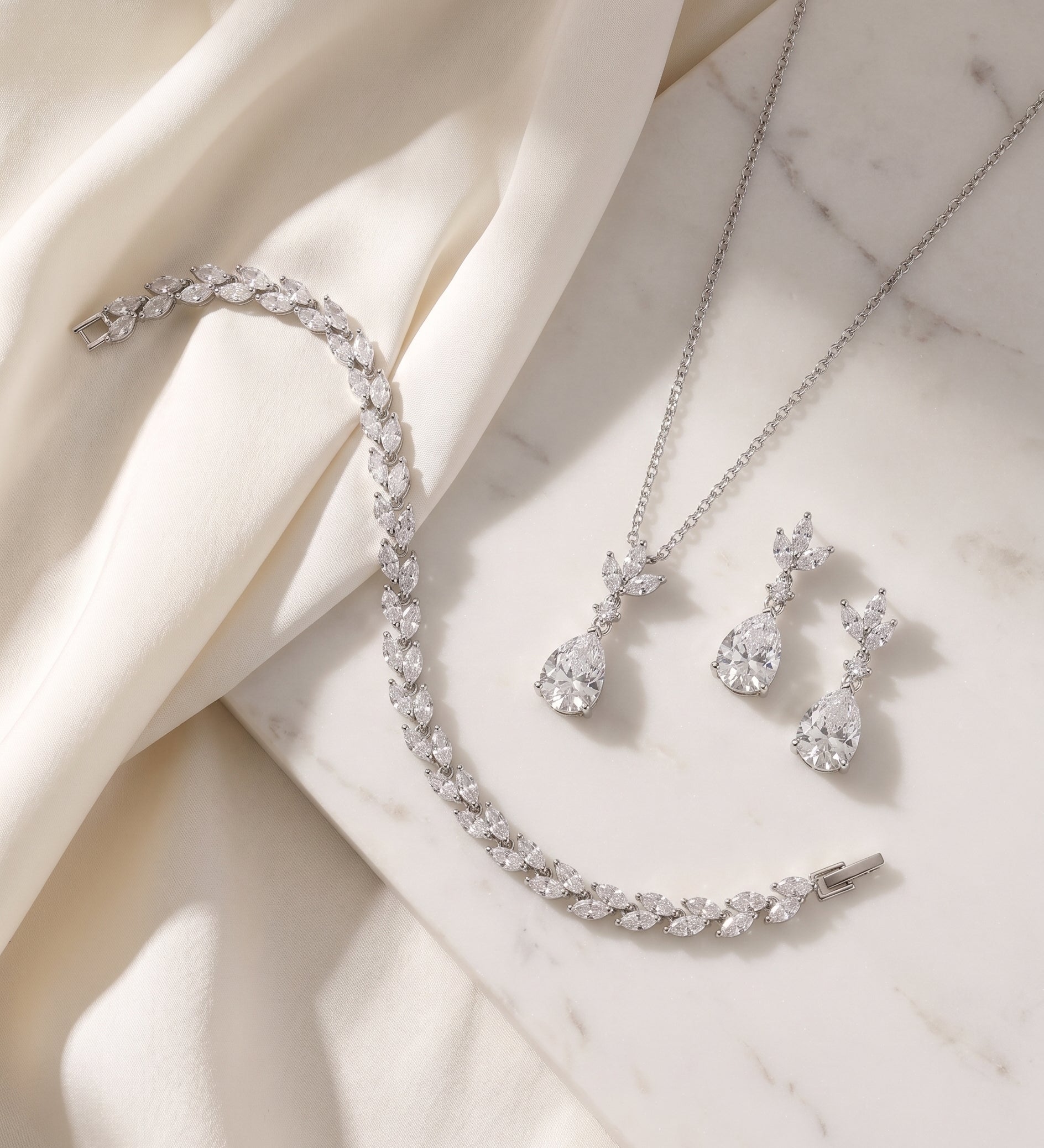 A delicate necklace, bracelet, and earrings are arranged on a white marble surface, creating an elegant and sophisticated display.
