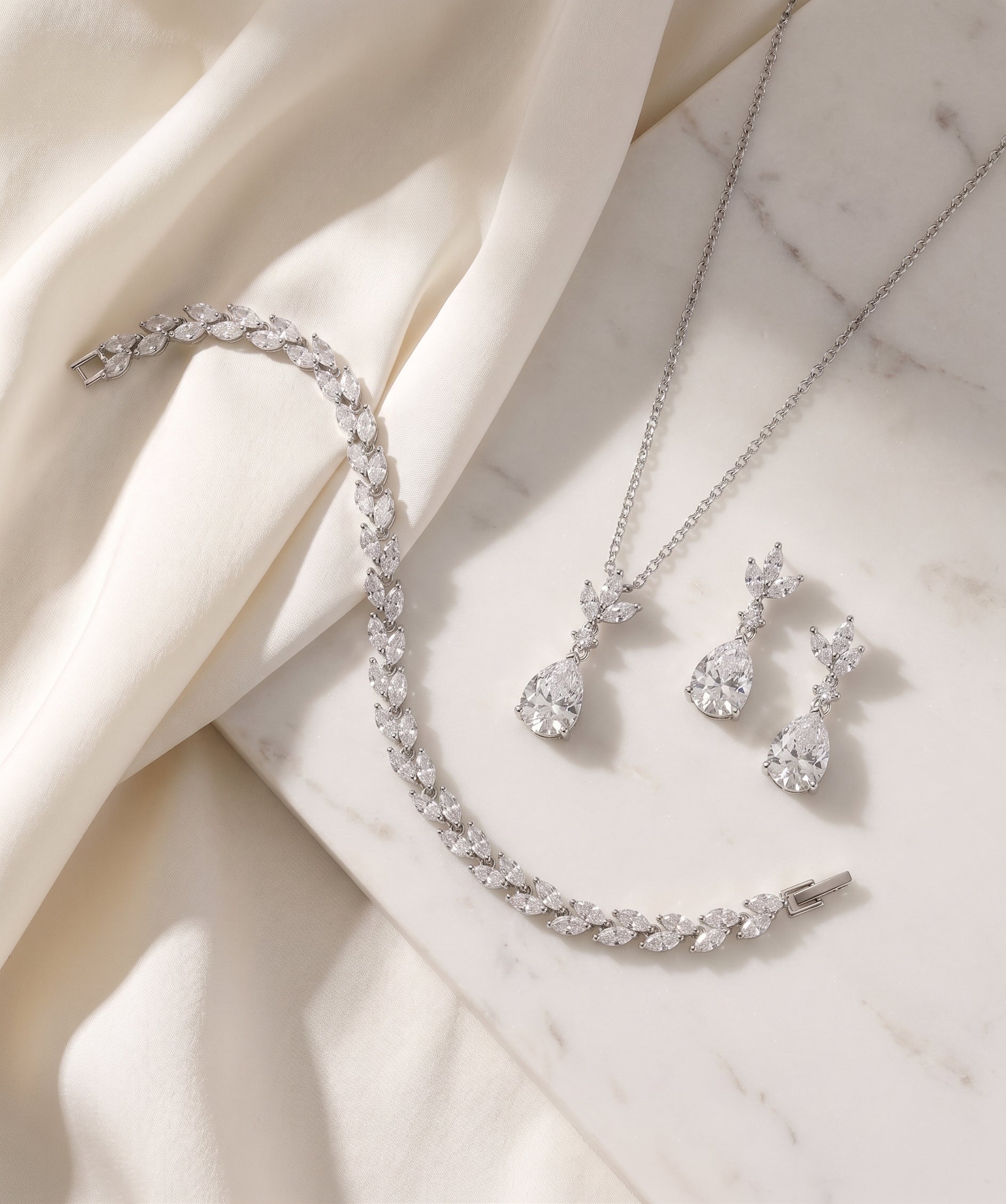 A delicate necklace, bracelet, and earrings are arranged on a white marble surface, creating an elegant and sophisticated display.