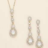 A gold necklace with a pendant and a pair of gold earrings with a pendant are displayed against a light beige background.