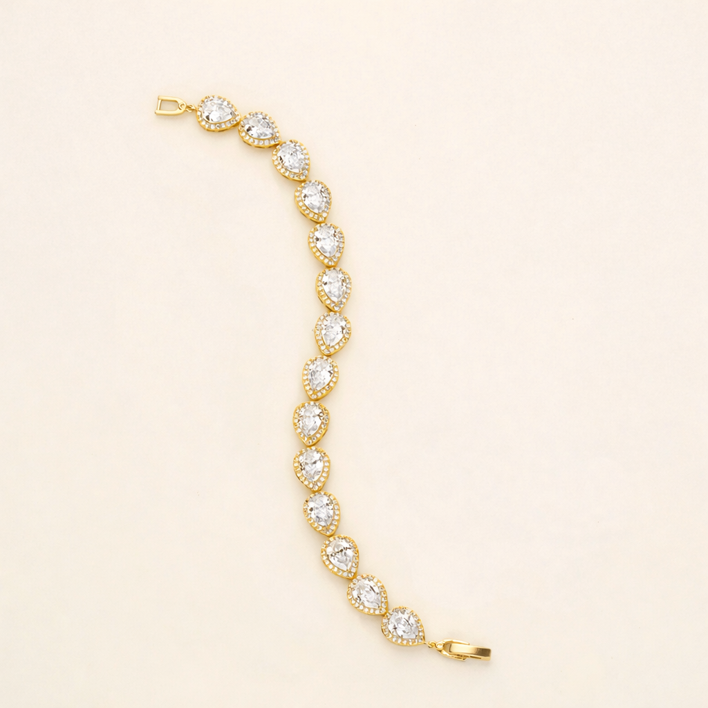 A gold bracelet with a row of small, clear gemstones on it, lying on a light-colored surface.