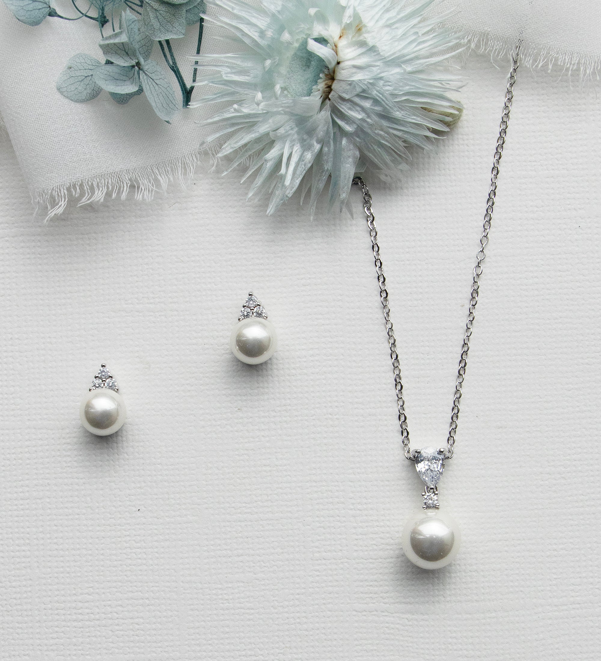 a necklace, earrings and a flower on a white surface