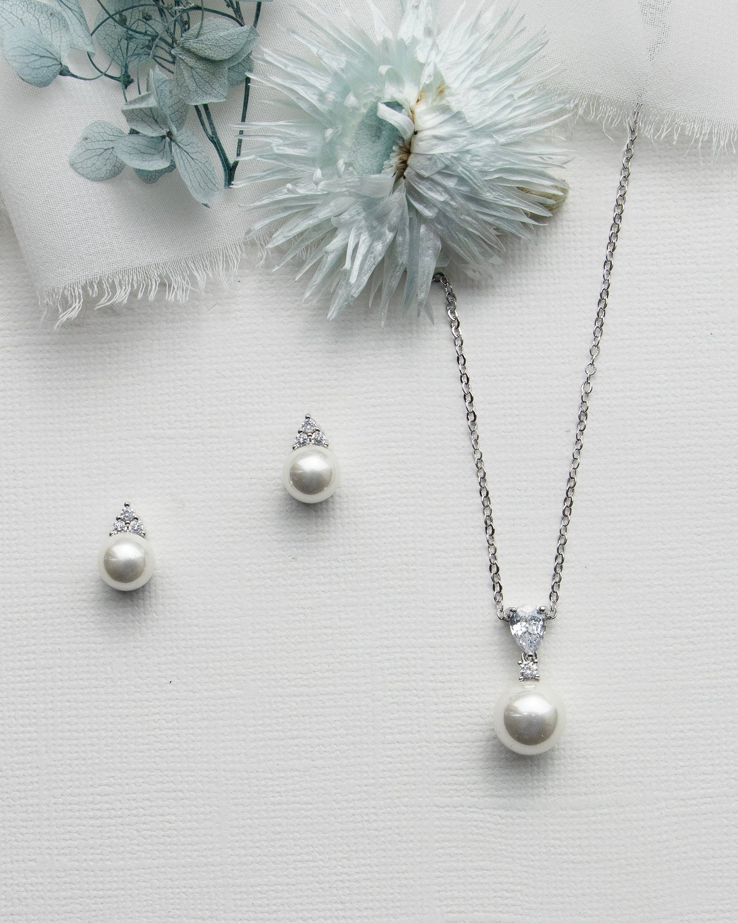 a necklace, earrings and a flower on a white surface