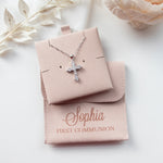 A necklace with a cross pendant is displayed in a beige box, accompanied by a small white flower and a personalized pouch with the name "Sophia" printed on it.