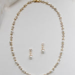 A delicate gold necklace with a row of small pearls and two dangling earrings are displayed on a white background.