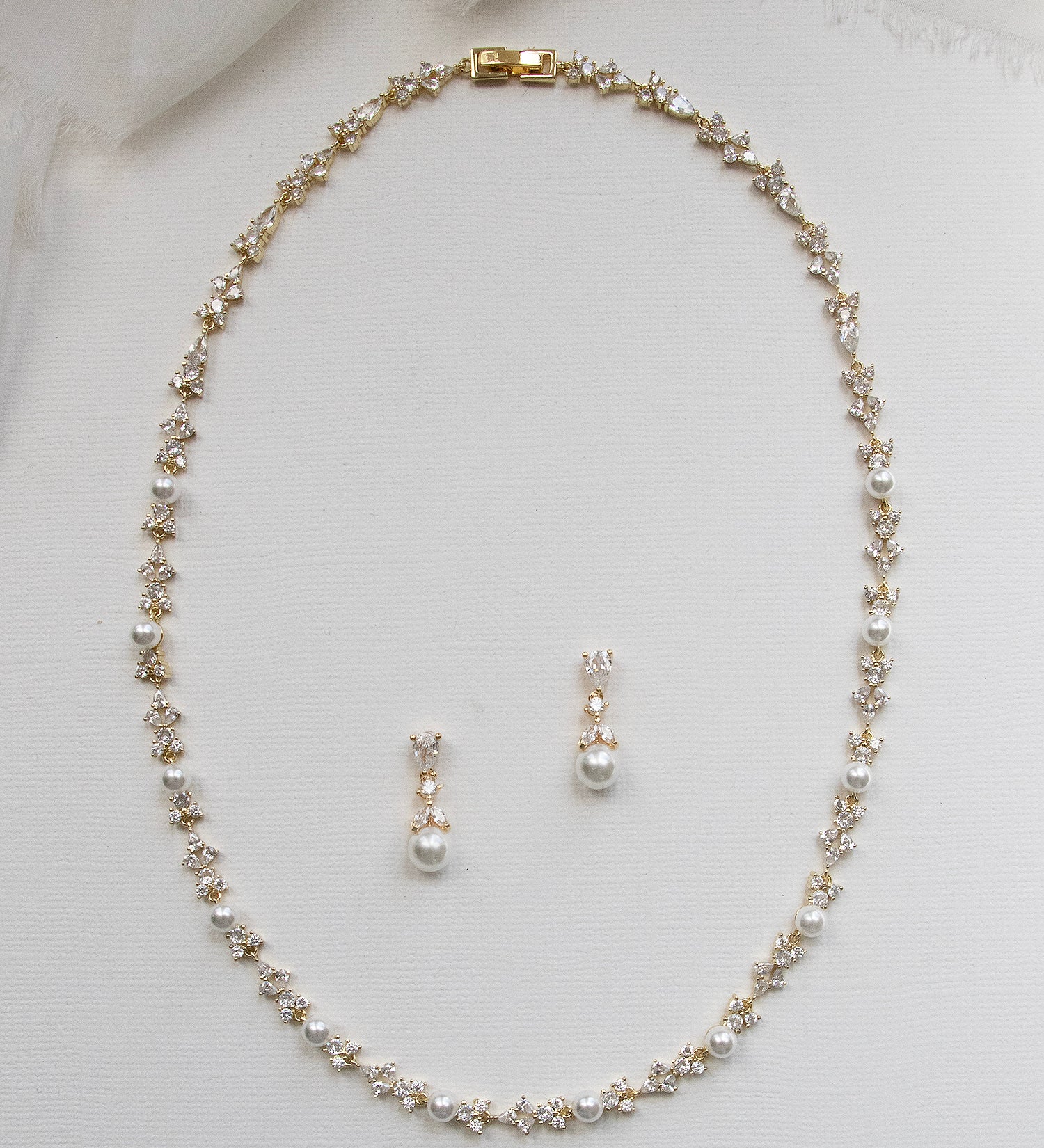 A delicate gold necklace with a row of small pearls and two dangling earrings are displayed on a white background.