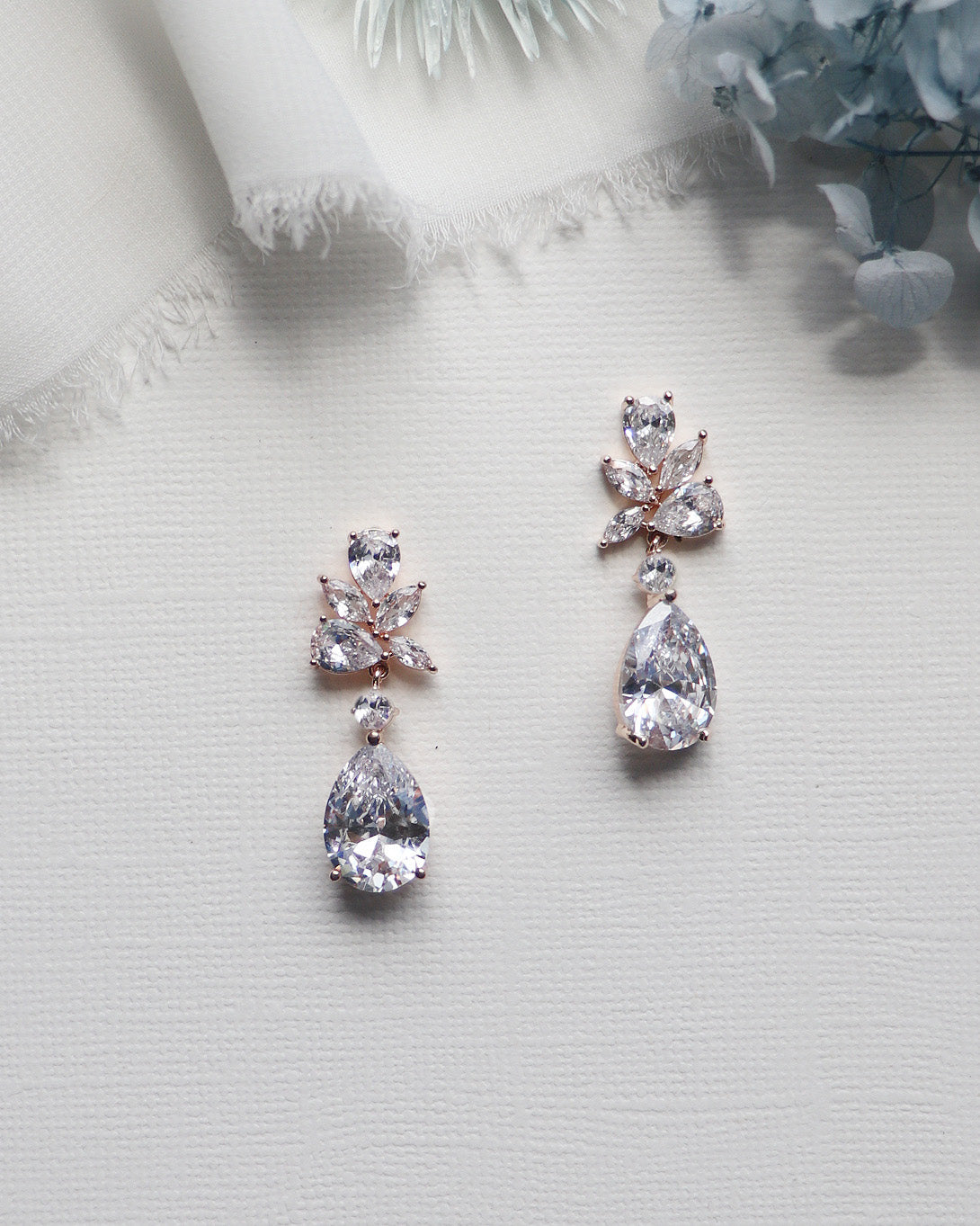 A pair of elegant diamond earrings with large, clear gemstones hanging from the earrings, placed on a white surface.