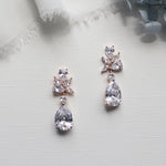 A pair of elegant diamond earrings with large, clear gemstones hanging from the earrings, placed on a white surface.