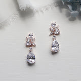 A pair of elegant diamond earrings with large, clear gemstones hanging from the earrings, placed on a white surface.