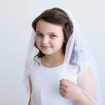 A young girl in a white dress and veil smiles at the camera.