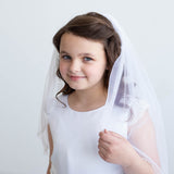 A young girl in a white dress and veil smiles at the camera.
