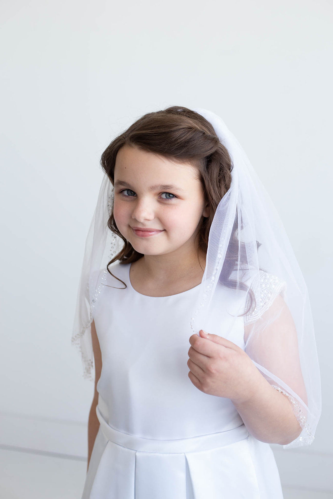 A young girl in a white dress and veil smiles at the camera.