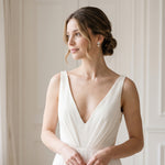 A woman in a white dress stands in a room, gazing off to the side with a thoughtful expression.