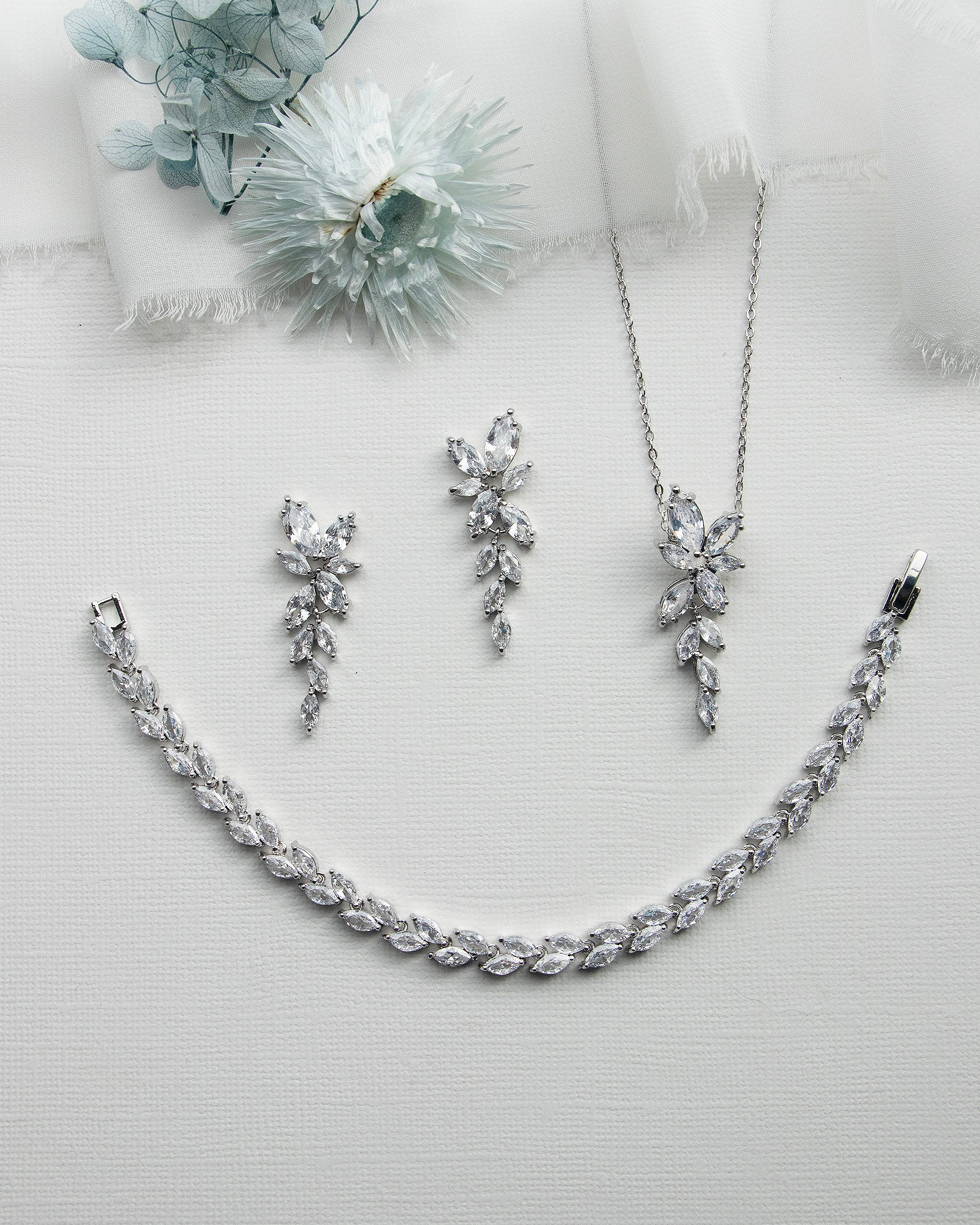 a necklace, earrings, and flower on a white surface