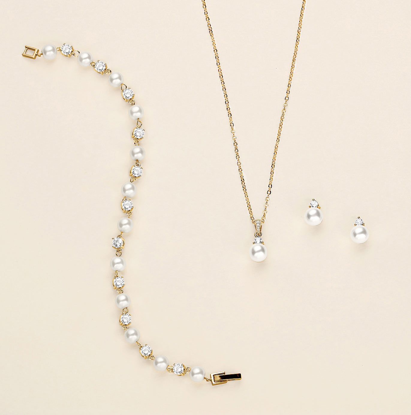 A delicate gold necklace with a pendant and earrings are displayed on a light beige background.