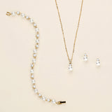 A delicate gold necklace with a pendant and earrings are displayed on a light beige background.