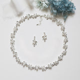 A delicate necklace with a leaf-shaped pendant, earrings, and a bracelet, all adorned with small white pearls and silver leaves, arranged on a white surface.