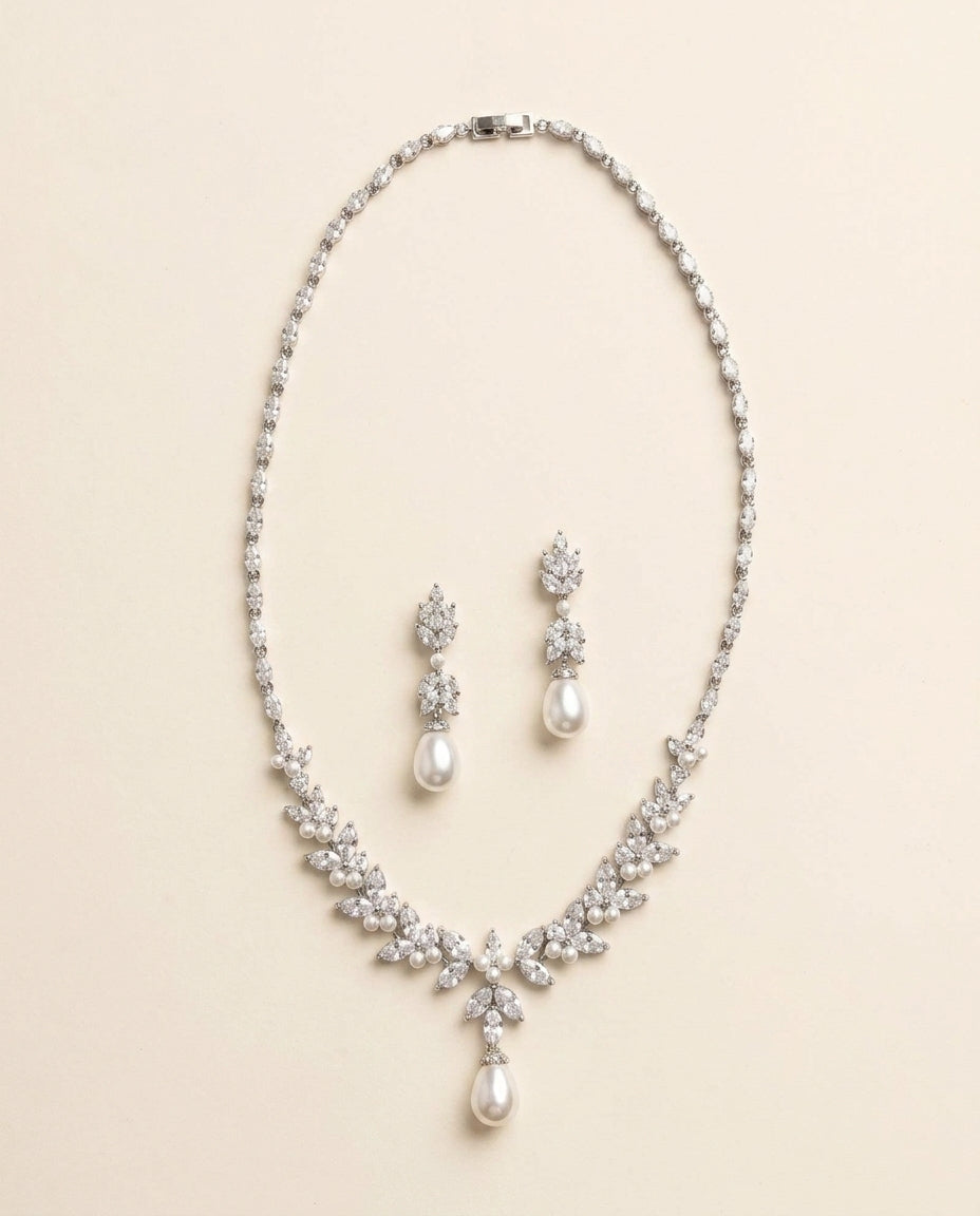 A necklace and earrings set made of white pearls and diamonds, arranged on a light-colored background.