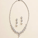 A necklace and earrings set made of white pearls and diamonds, arranged on a light-colored background.