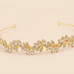 A gold-colored tiara adorned with numerous small, clear gemstones arranged in a decorative pattern.