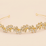 A gold-colored tiara adorned with numerous small, clear gemstones arranged in a decorative pattern.