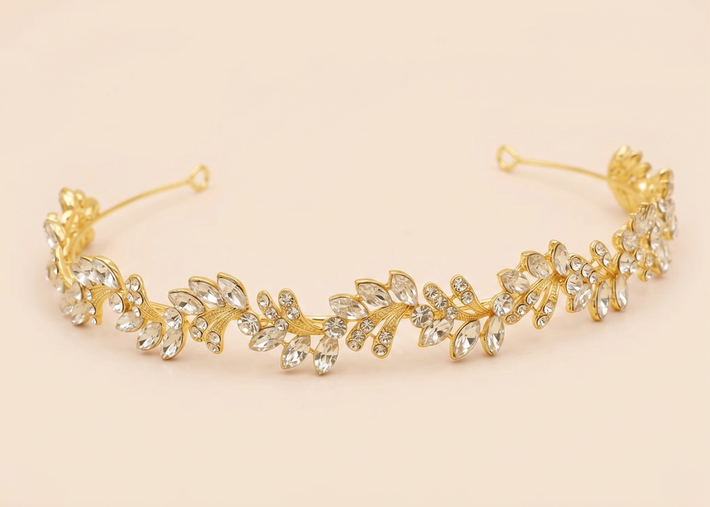 A gold-colored tiara adorned with numerous small, clear gemstones arranged in a decorative pattern.