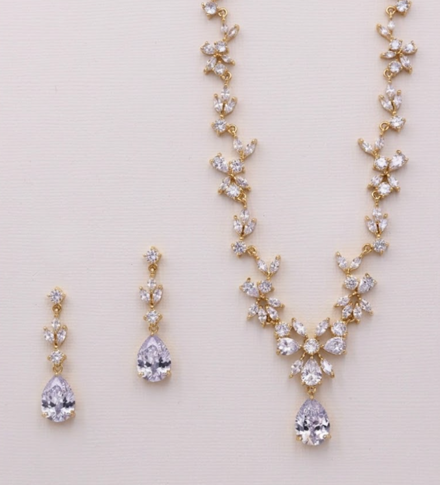 A necklace and earrings set made of gold and clear gemstones, including pear-shaped and round-shaped stones.