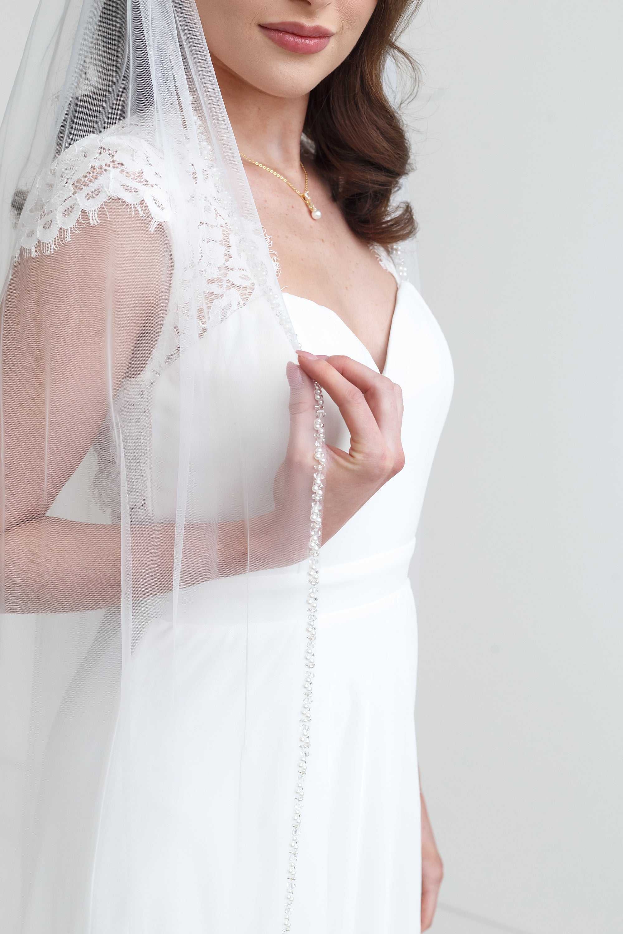 A woman in a white wedding dress with a long veil stands against a white background.