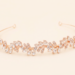 A gold-colored tiara adorned with numerous small, clear gemstones arranged in a decorative pattern.