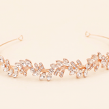 A gold-colored tiara adorned with numerous small, clear gemstones arranged in a decorative pattern.