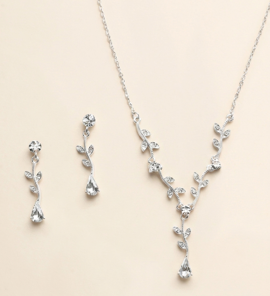 A necklace and earrings set made of silver and clear gemstones, including a pendant with a leaf design and dangling earrings with clear gemstones.