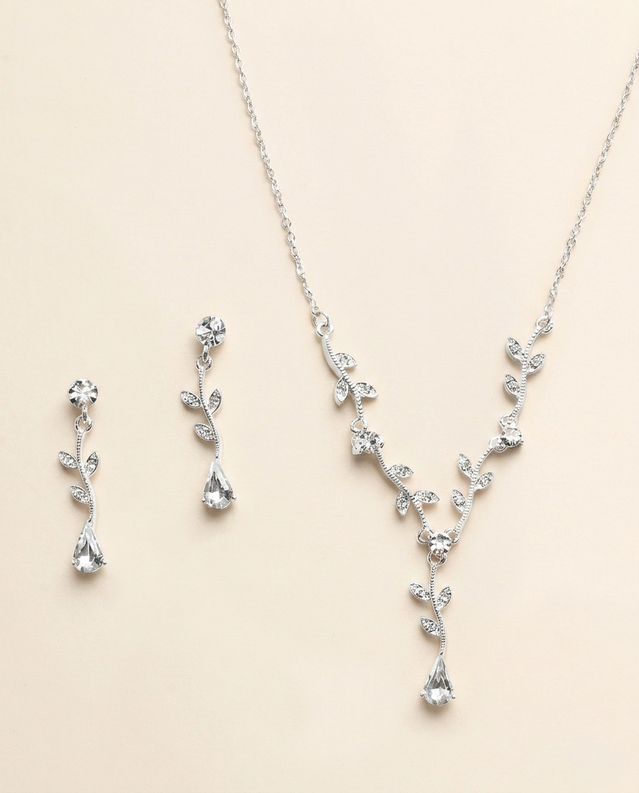A necklace and earrings set made of silver and clear gemstones, including a pendant with a leaf design and dangling earrings with clear gemstones.
