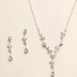 A necklace and earrings set made of silver and clear gemstones, including a pendant with a leaf design and dangling earrings with clear gemstones.