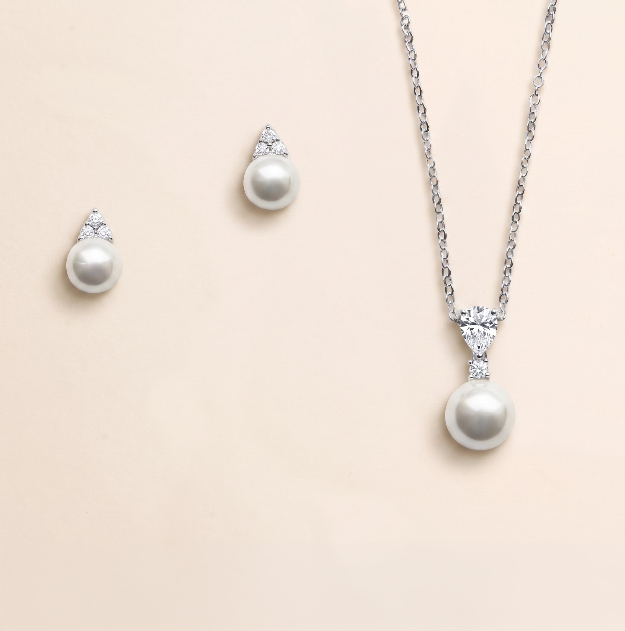 A necklace and earrings set made of silver and white pearls, with a pendant featuring a large round pearl and smaller pearls.