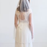 A woman wearing a white wedding dress with a veil, standing against a white background.