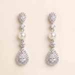A pair of elegant earrings with pearls and diamonds, set against a light beige background.