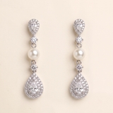 A pair of elegant earrings with pearls and diamonds, set against a light beige background.