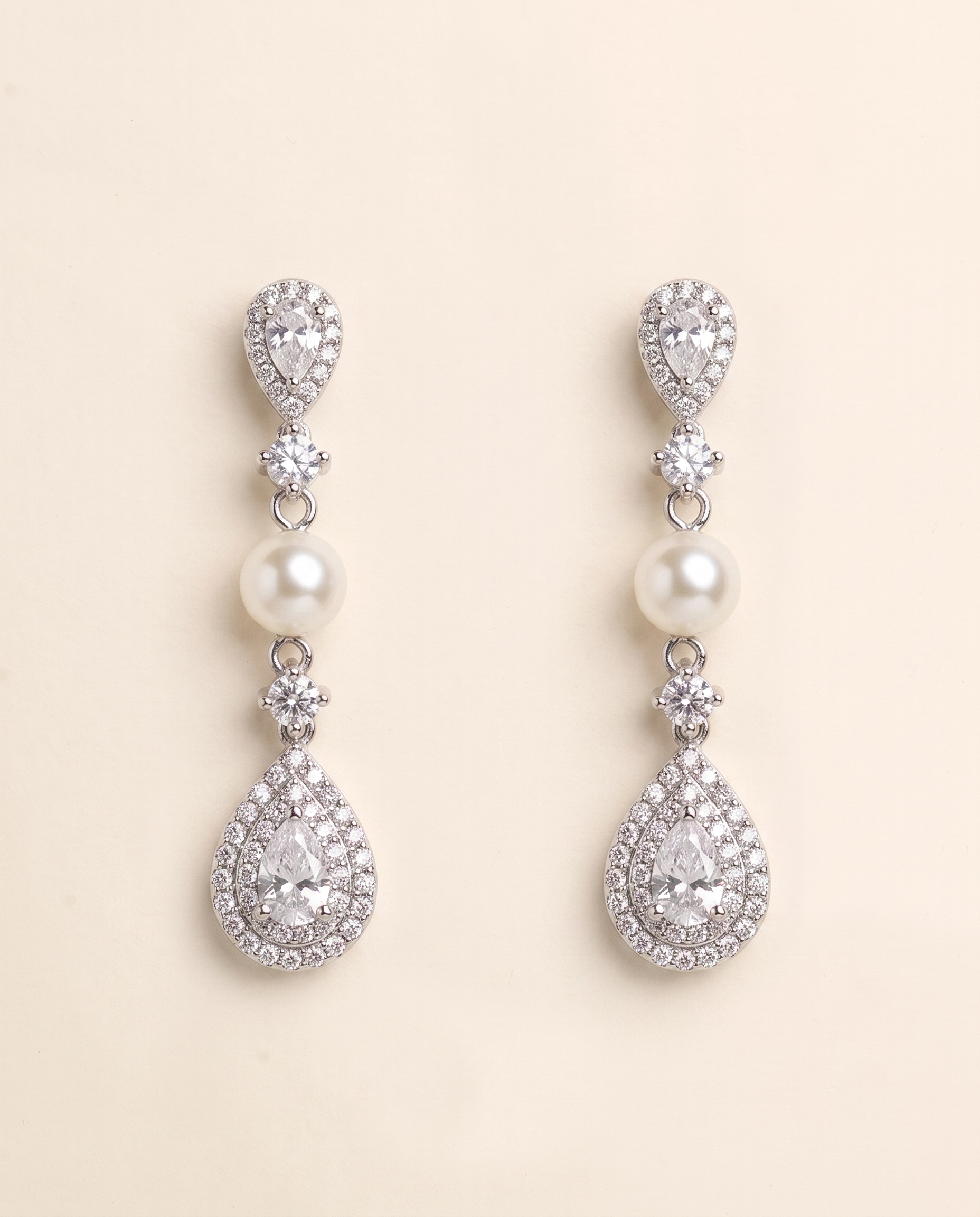 A pair of elegant earrings with pearls and diamonds, set against a light beige background.
