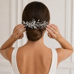 A woman in a white dress is adjusting her hair accessory, which is a decorative hair clip with small flowers or leaves attached to it.