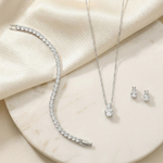 A collection of elegant jewelry, including a necklace, bracelet, earrings, and a pendant, is displayed on a white marble surface.