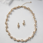 A delicate gold necklace with leaf-shaped pendants and earrings is displayed on a white background.