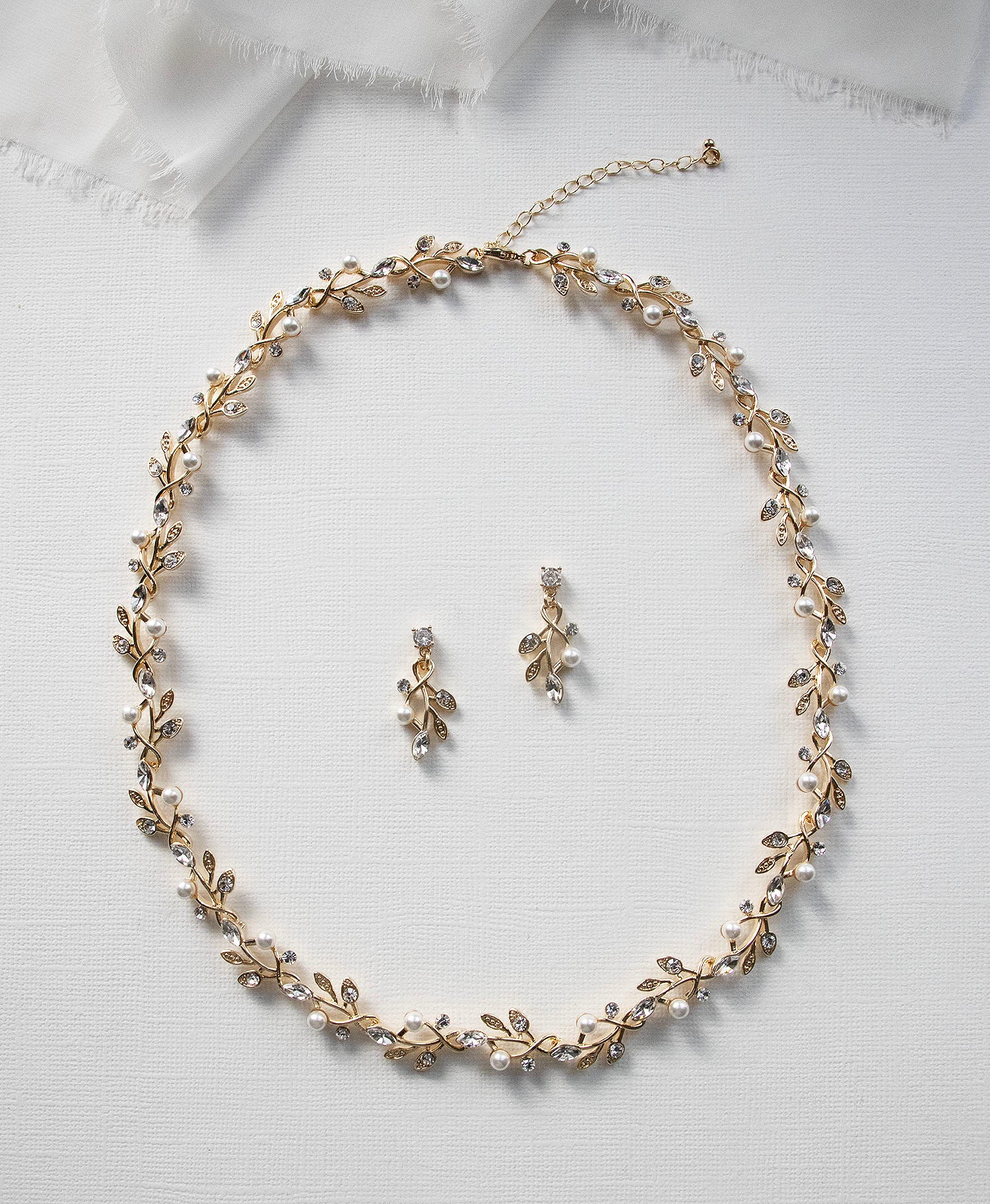 A delicate gold necklace with leaf-shaped pendants and earrings is displayed on a white background.