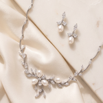 A necklace and earrings set made of white pearls and diamonds, placed on a white fabric background.