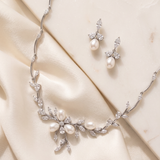 A necklace and earrings set made of white pearls and diamonds, placed on a white fabric background.