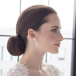 A woman with a bun hairstyle wearing a white lace top and large dangling earrings, looking to the side with a neutral expression.