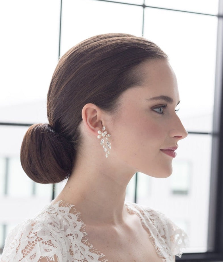 A woman with a bun hairstyle wearing a white lace top and large dangling earrings, looking to the side with a neutral expression.