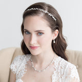 A woman with long brown hair wearing a white lace dress and a headband with small white flowers, smiling at the camera.